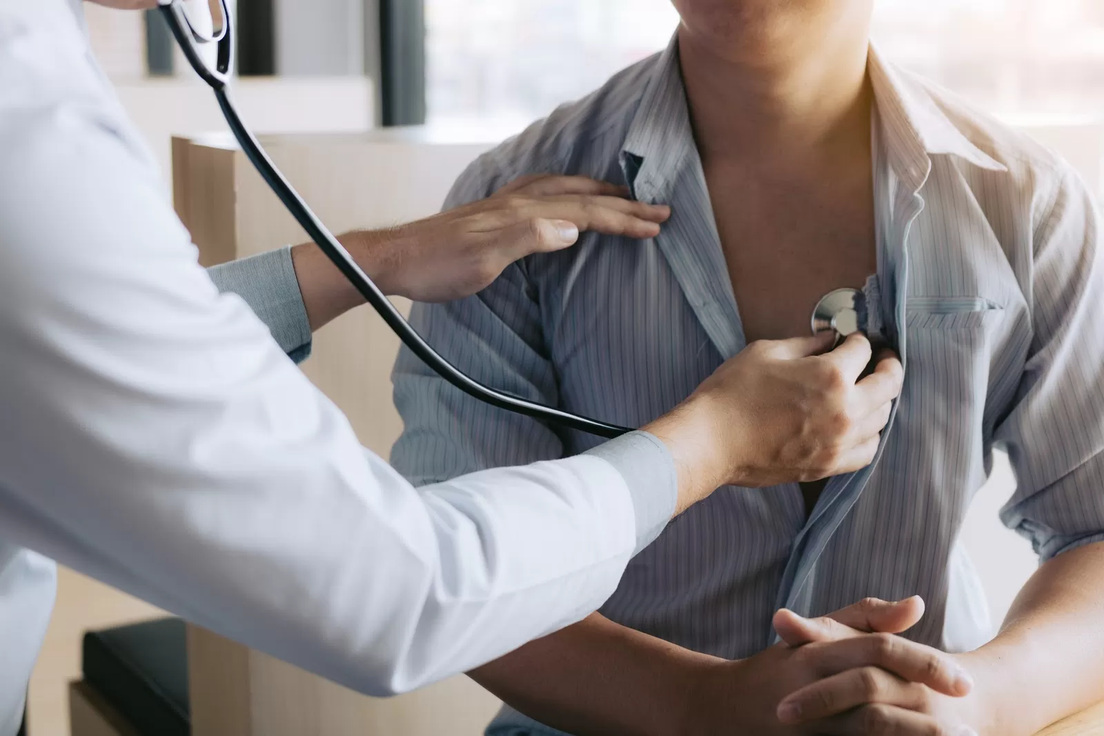 Doctor using a stethoscope to listen to a male patient’s heartbeat during a medical exam.