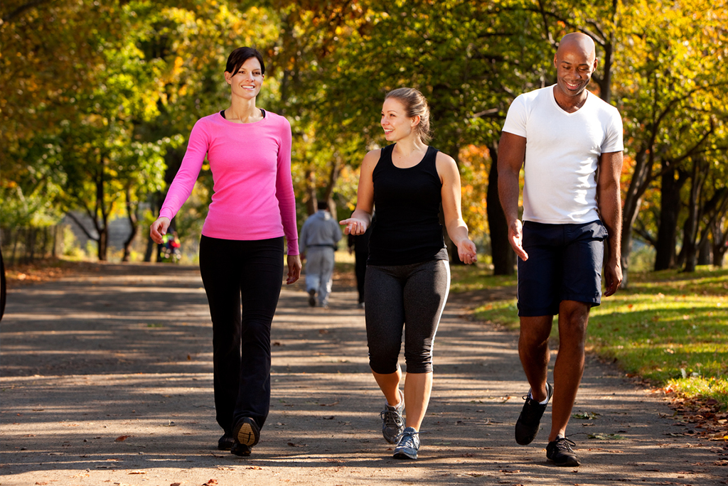 Three people walking outdoors for health benefits through a park wearing exercise clothing
