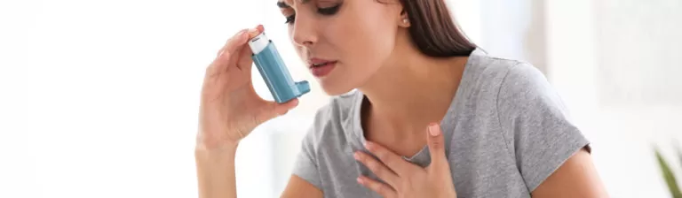 Woman experiencing difficulty breathing and using an inhaler to relieve allergy or asthma symptoms.