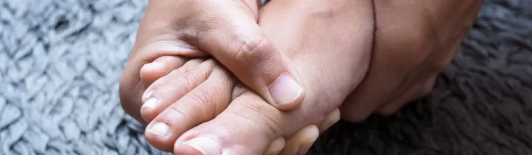 Person firmly holding their foot in pain, showing symptoms of gout or joint inflammation.