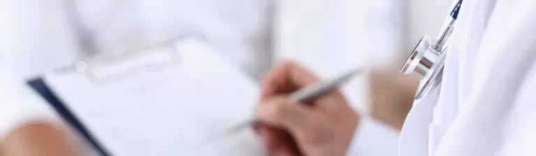 Doctor writing notes on a medical chart or clipboard during a patient consultation.