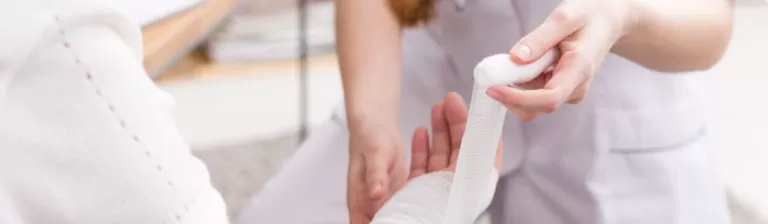 Healthcare provider wrapping a male patient’s hand with medical bandages during treatment for an injury.